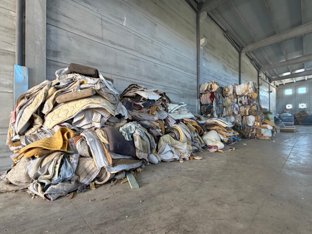 La Generalitat ha reciclat 5.441 matalafs afectats per les riuades d’octubre de 2024 mitjançant una tecnologia de l’empresa valenciana Ecoaqua que, segons l’administració autonòmica, permet recuperar el 100% dels materials i reincorporar-los al cicle productiu. El vicepresident tercer i conseller de Medi Ambient, Infraestructures, Territori i de la Recuperació, Vicente Martínez Mus, ha explicat el procés durant una visita a les instal·lacions d’Ontinyent, acompanyat de l’alcalde, Jorge Rodríguez. Martínez Mus ha assenyalat que l’empresa “utilitza una tecnologia de reciclatge basada en aigua a ultrapressió que permet separar els diferents materials”. Separació dels matalafs en els punts de transferència de l’Horta La recuperació ha sigut possible gràcies a la separació dels residus en els punts de transferència de Catarroja, Picassent i Quart de Poblet, així com en una instal·lació de l’Entitat Metropolitana per al Tractament de Residus. Els matalafs formaven part dels materials que calia gestionar després de la riada per a evitar que acabaren en abocadors, juntament amb pneumàtics, bombones de butà, extintors i plàstics. El vicepresident ha recordat que les inundacions van generar més d’un milió de tones de residus i que la Generalitat va destinar més de 200 milions d’euros a un pla de xoc per a gestionar-los. La retirada de materials també es va estendre als espais naturals afectats, com mostra la neteja de 2.475 tones de residus de l’Albufera després de la DANA. Ferralla, escumes i tèxtils tornen al cicle productiu El sistema separa els components dels matalafs per a donar-los nous usos. La ferralla s’envia a foneries per al seu aprofitament industrial, mentre que les escumes es processen i reutilitzen. Els tèxtils i les mescles de materials es transformen en aïllants i components destinats a fabricar nous matalafs. L’EMTRE ja havia donat a conéixer el procés de reciclatge d’Ecoaqua, basat en la recuperació de materials dels matalafs usats per a obtindre matèries primeres secundàries. Martínez Mus ha destacat que el projecte mostra la importància de la col·laboració per a passar de la resposta inicial a la DANA a una gestió dels residus que prioritze la recuperació i la reutilització dels materials.